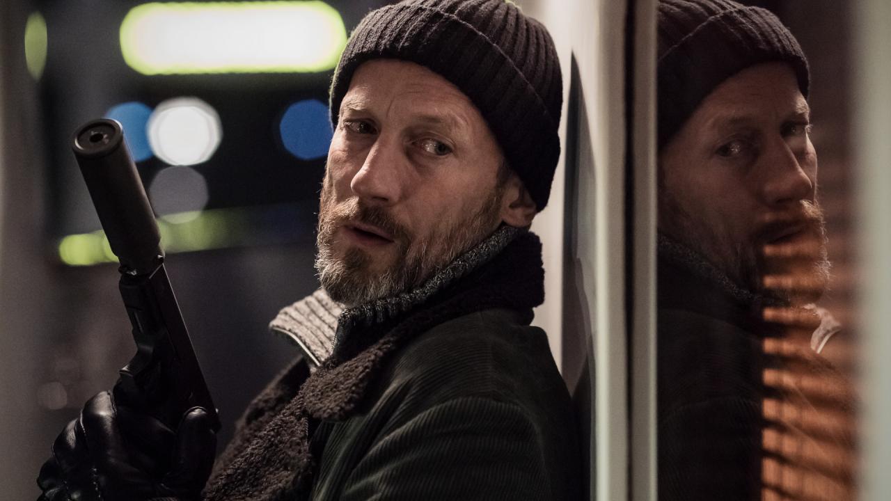 West of Liberty, Szenenbild: Nachts: Ein Mann lehnt mit einer Waffe in der Hand an einer Fensterscheibe.