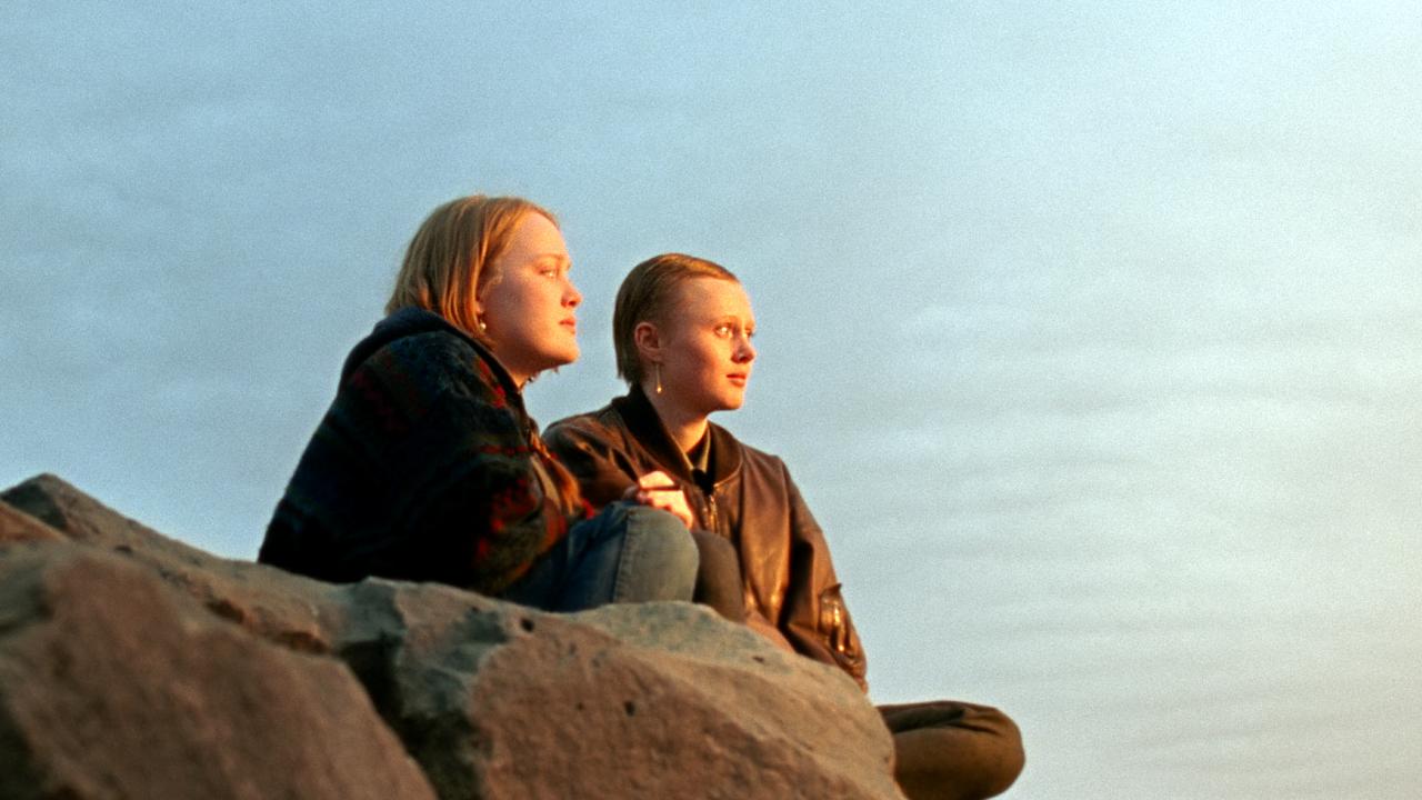 Still aus dem Drama WENN DAS LICHT ZERBRICHT: Zwei jungen Frauen sitzen vor weitem Himmel auf einem Felsen und blicken nach rechts in die Ferne.