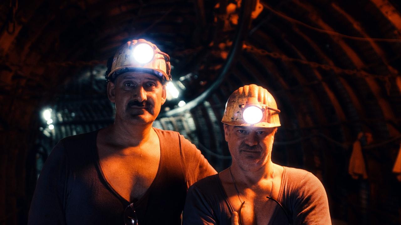 Filmstill aus dem Dokumentarfilm WIR WAREN KUMPEL: Zwei Bergarbeiter stehen nebeneinander in einem dunklem Schacht. Sie tragen Helme mit Lampen.
