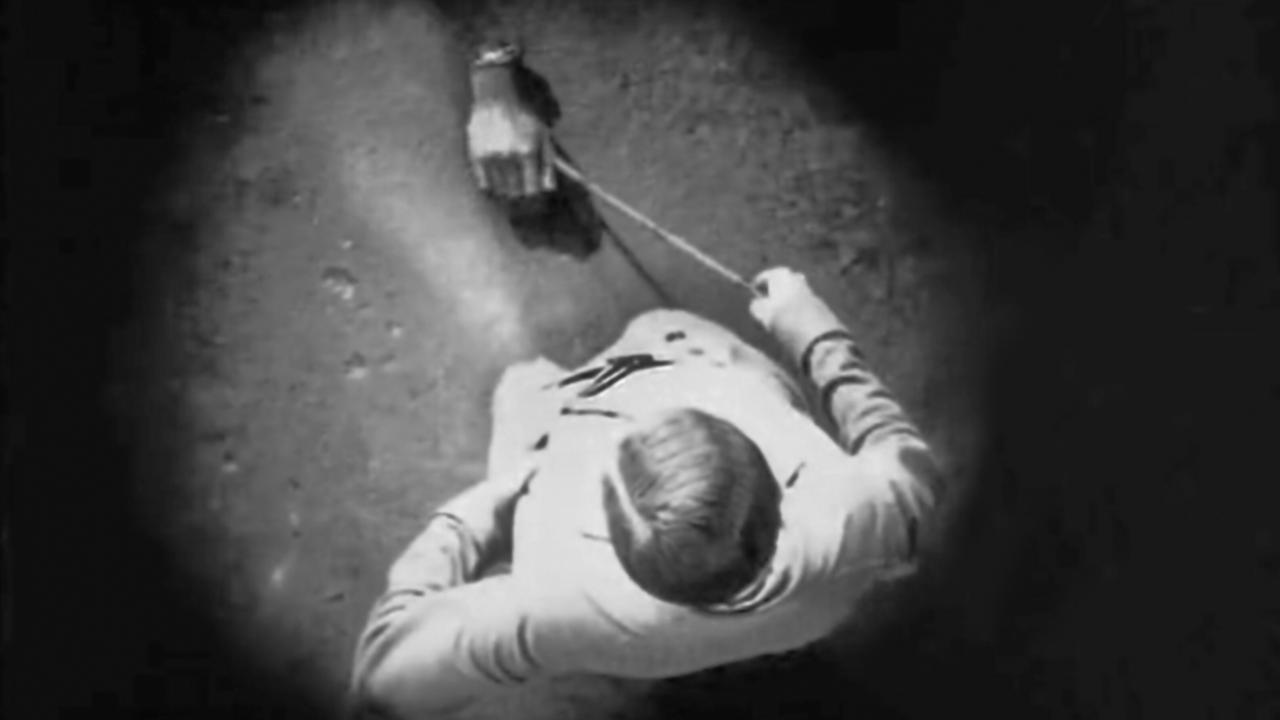 Filmstill aus EIN ANADLUSISCHER HUND: Die Kamera blickt von oben auf einen Mann, der eine Hand an einer Leine ausführt.