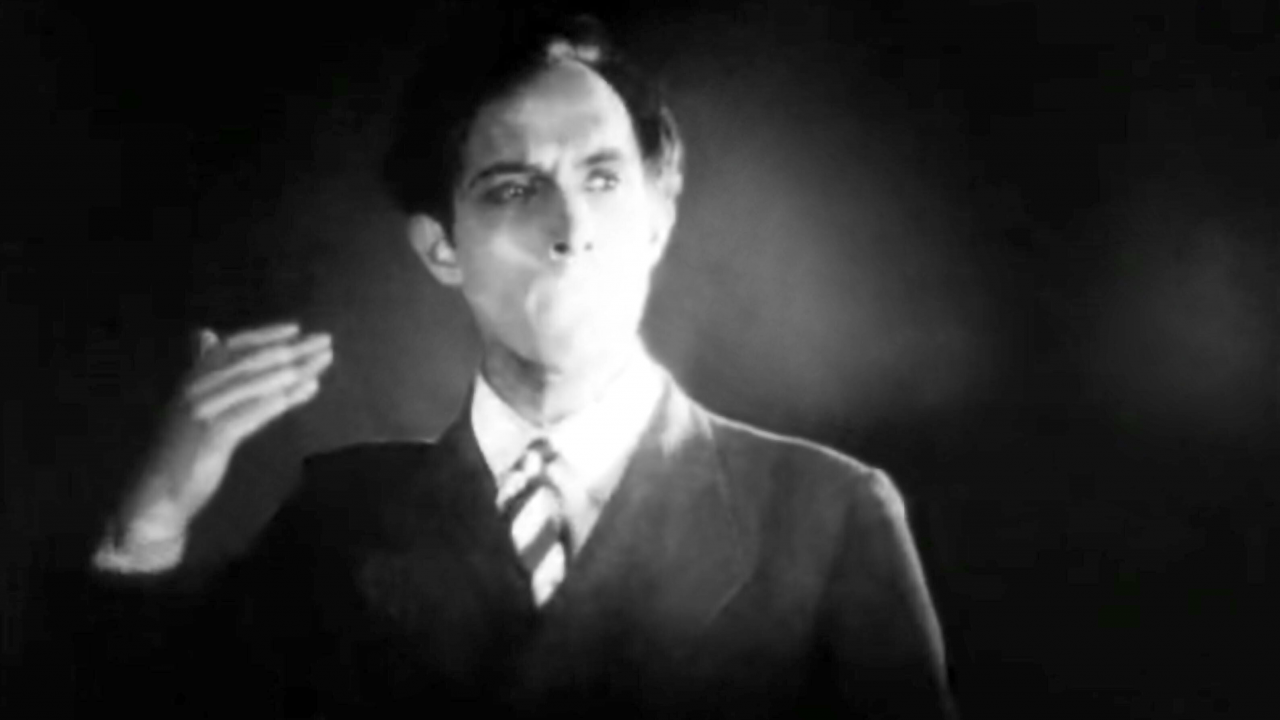 Filmstill aus EIN ANADLUSISCHER HUND: Porträt eines Mannes ohne Mund. Er hält seine rechte Hand erhoben.