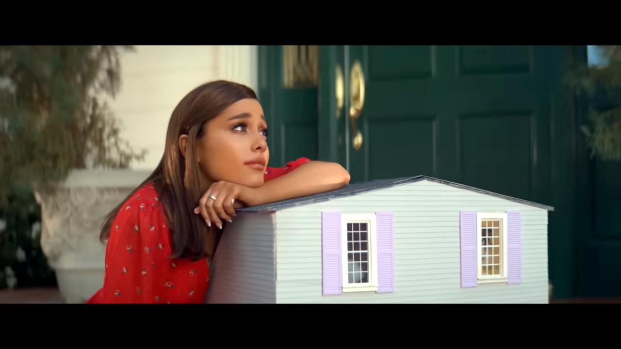 Still aus dem Musikvideo THANK U, NEXT von Ariana Grande: Sie Sängerin lehnt sich auf ein Puppenhaus und blickt nachdenklich in die Ferne.