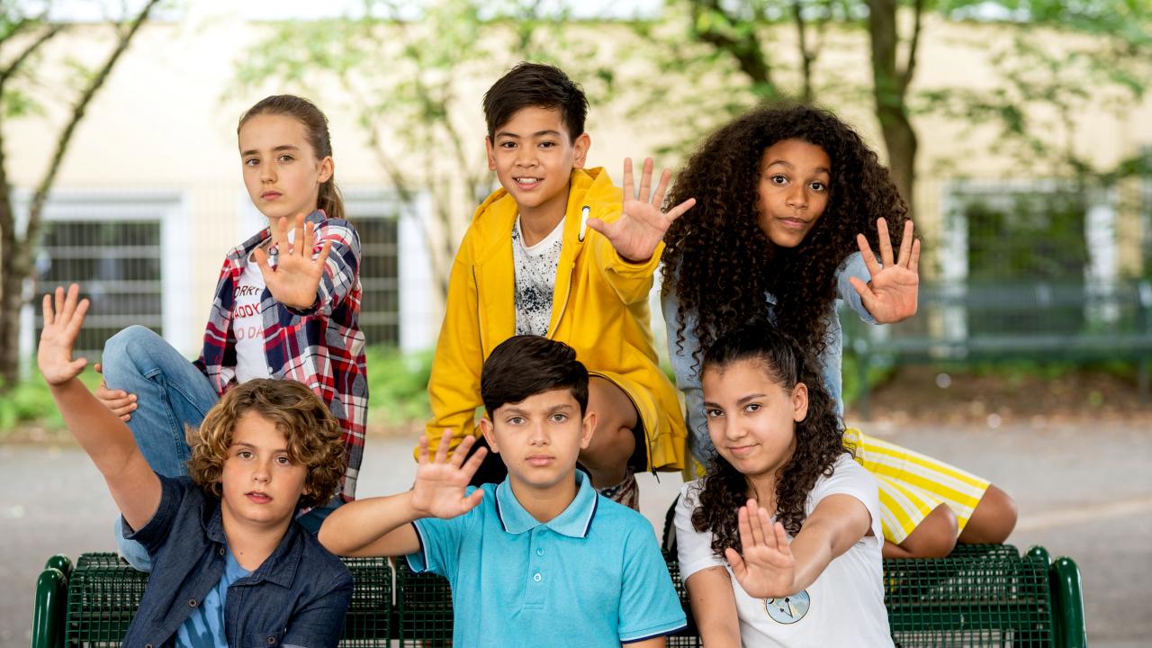 Promobild zur KiKA-Serie MOOOMENT!: Drei Mädchen und drei Jungen sitzen auf einer Bank und halten eine Hand wie zum Stoppen nach vorn.