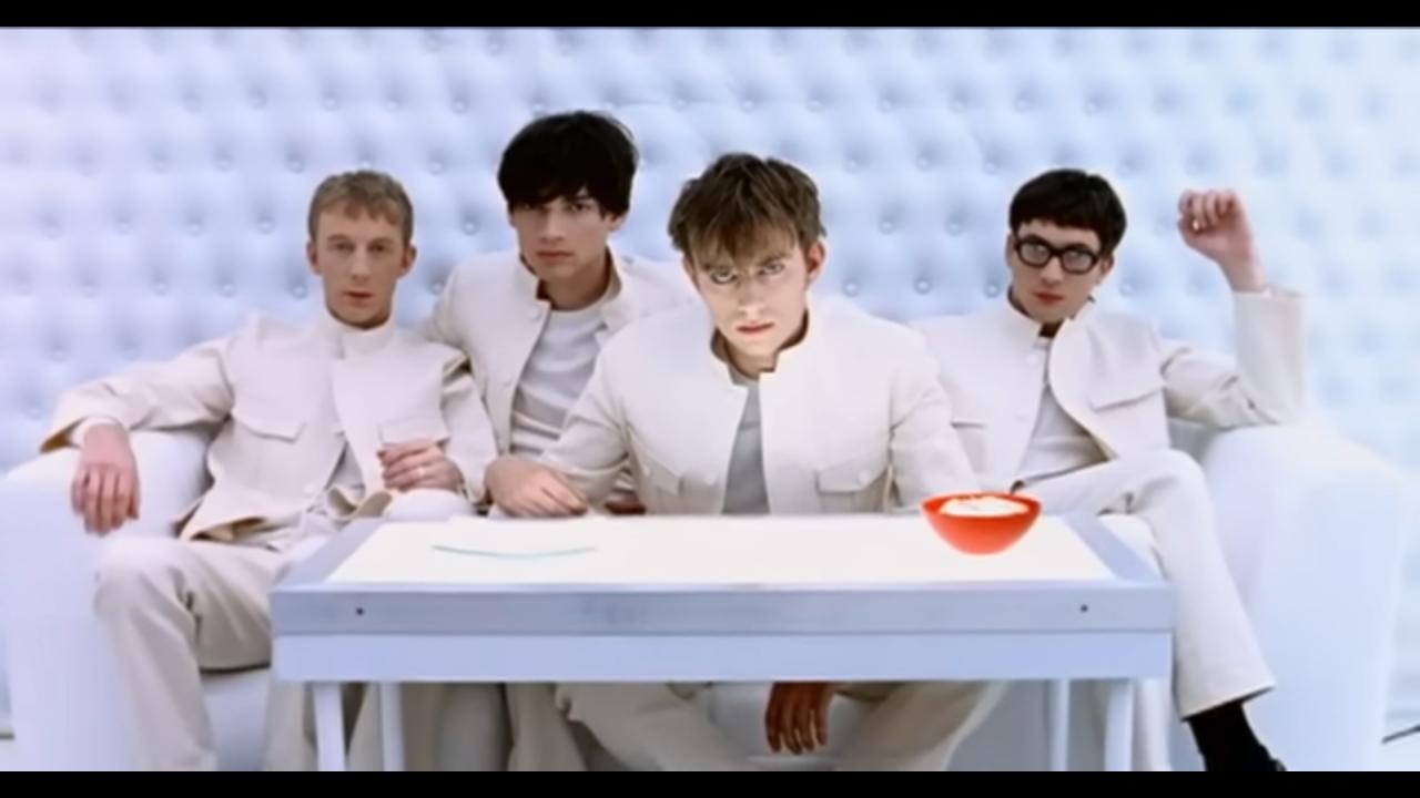 Still aus dem Musikvideo THE UNIVERSAL von Blur: Die vier Musiker der Band sitzen weiß gekleidet vor einer weißen Wand – ähnlich wie die Hauptfiguren in dem Film UHRWERK ORANGE (1971) von Stanley Kubrick