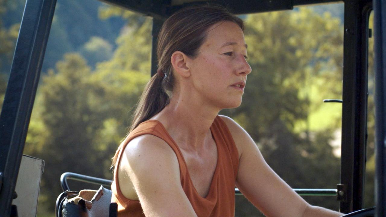 Still aus dem Drama MILCH INS FEUER: Halbnahe Aufnahme einer Frau, die in einem Traktor sitzt.