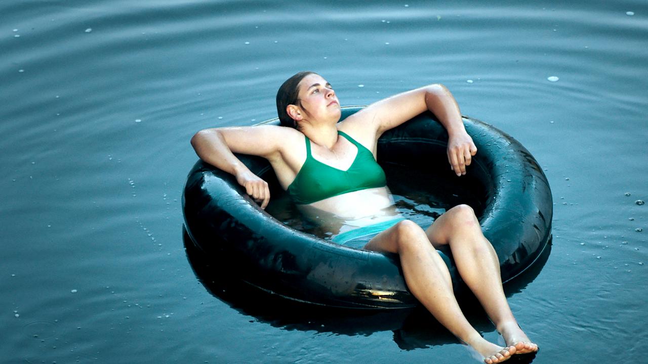 Still aus dem Drama MILCH INS FEUER: Eine junge Frau im grünen Bikini liegt in einem großen Schwimmreifen im Wasser.