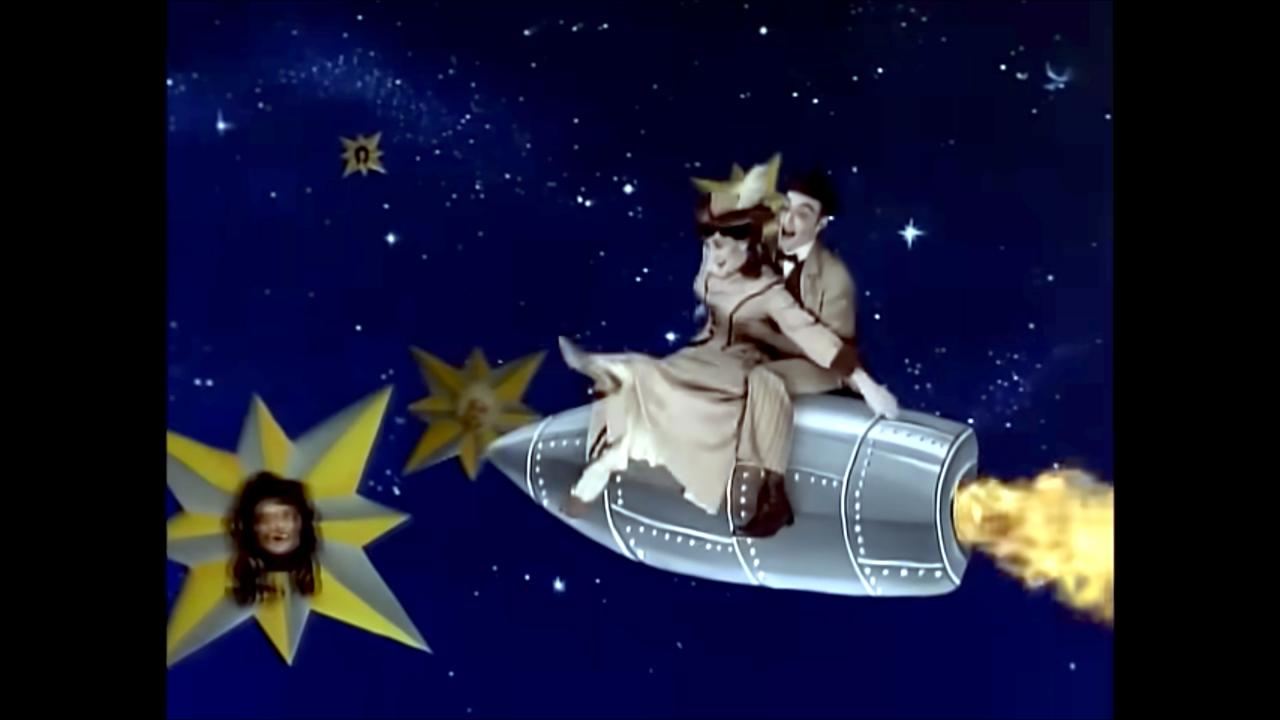 Still aus dem Musikvideo TONIGHT, TONIGHT von The Smashing Pumpkins: Eine Frau und ein Mann, gekleidet im Stil um 1900, sitzen auf einer stilisierten Rakete im Weltall. 