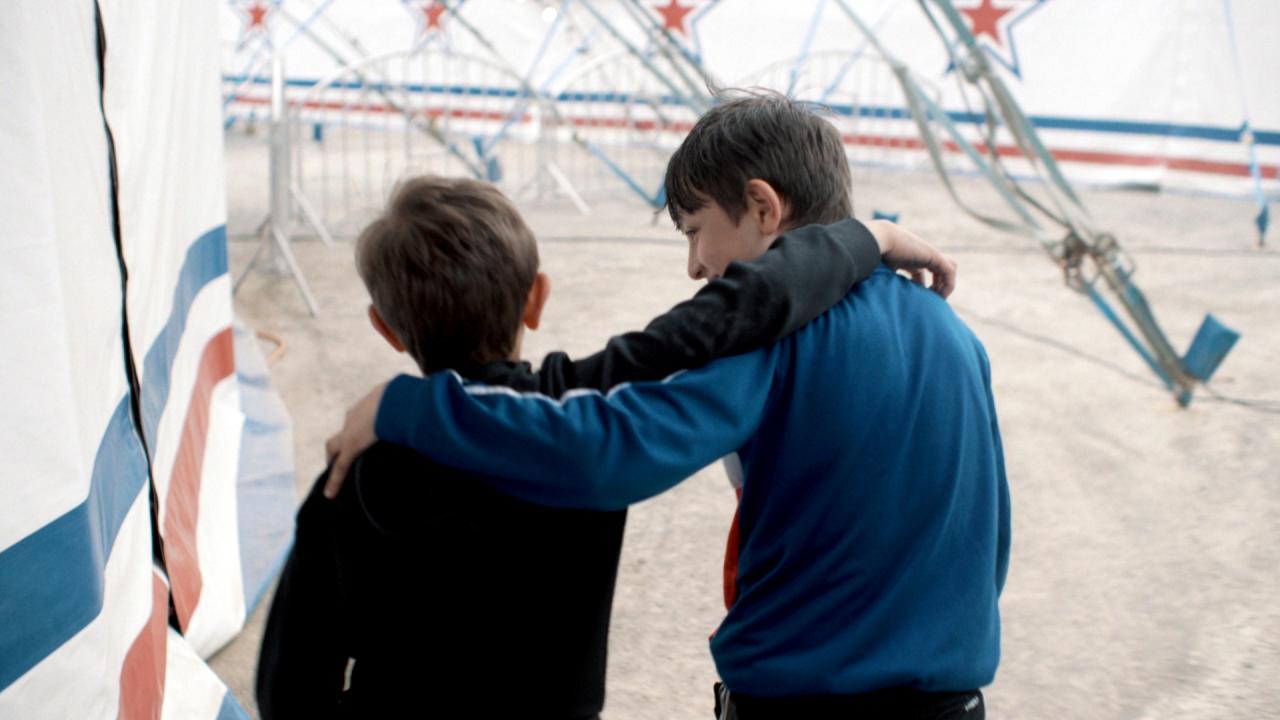 Still aus dem Dokumentarfilm ZIRKUSKIND: Zwei Jungen im Grundschulalter laufen neben einem Zirkuszelt. Sie sind von hinten zu sehen.