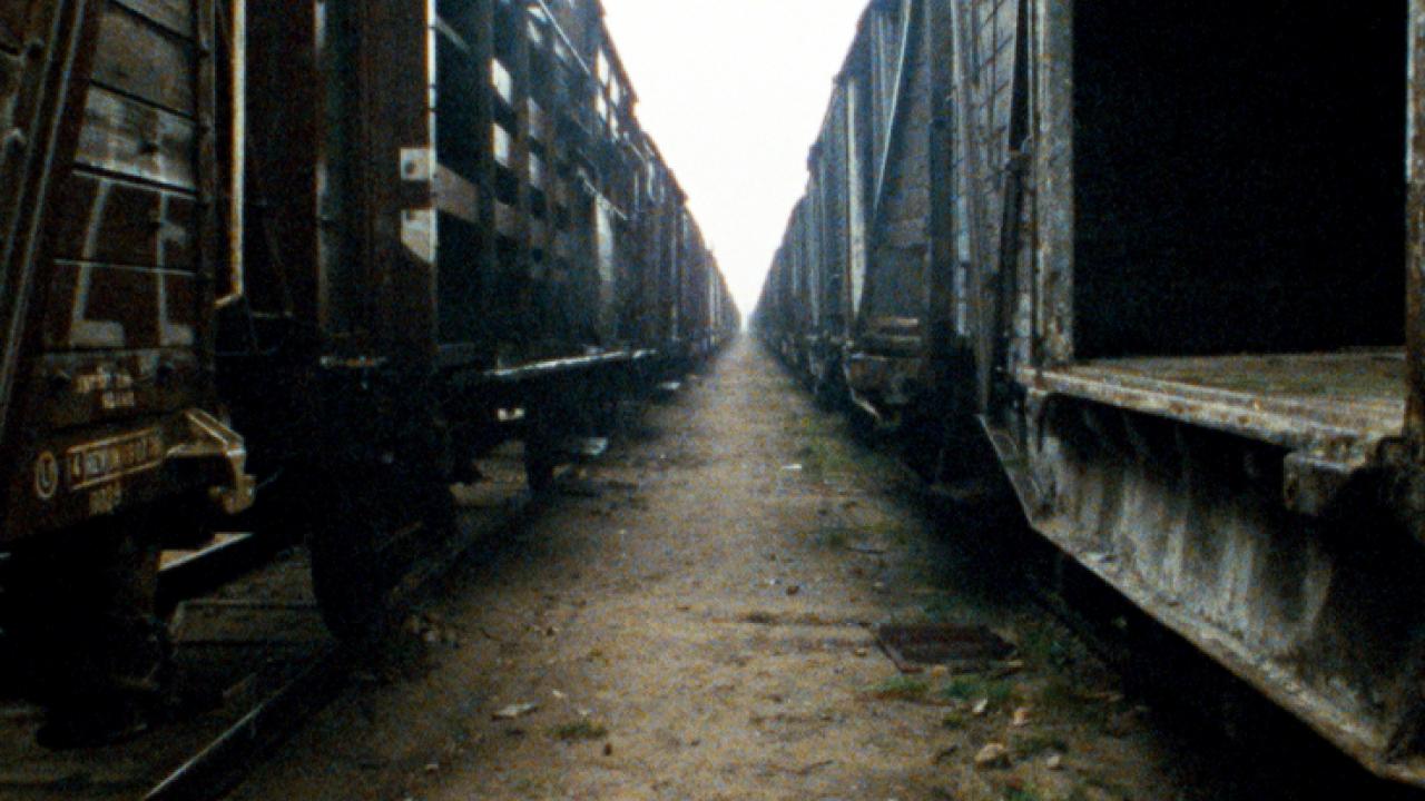 Filmstill aus dem Dokumentarfilm SHOAH: ein endlos wirkender Gang zwischen zwei Güterzügen