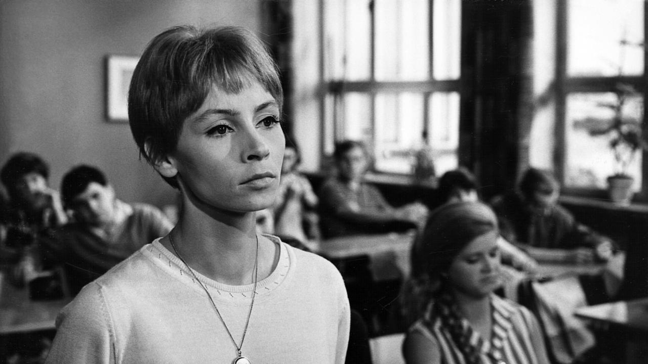 Filmstill aus dem DEFA-Drama KARLA: Eine junge, kurzhaarige Frau steht in einem Klassenraum und schaut ernst.