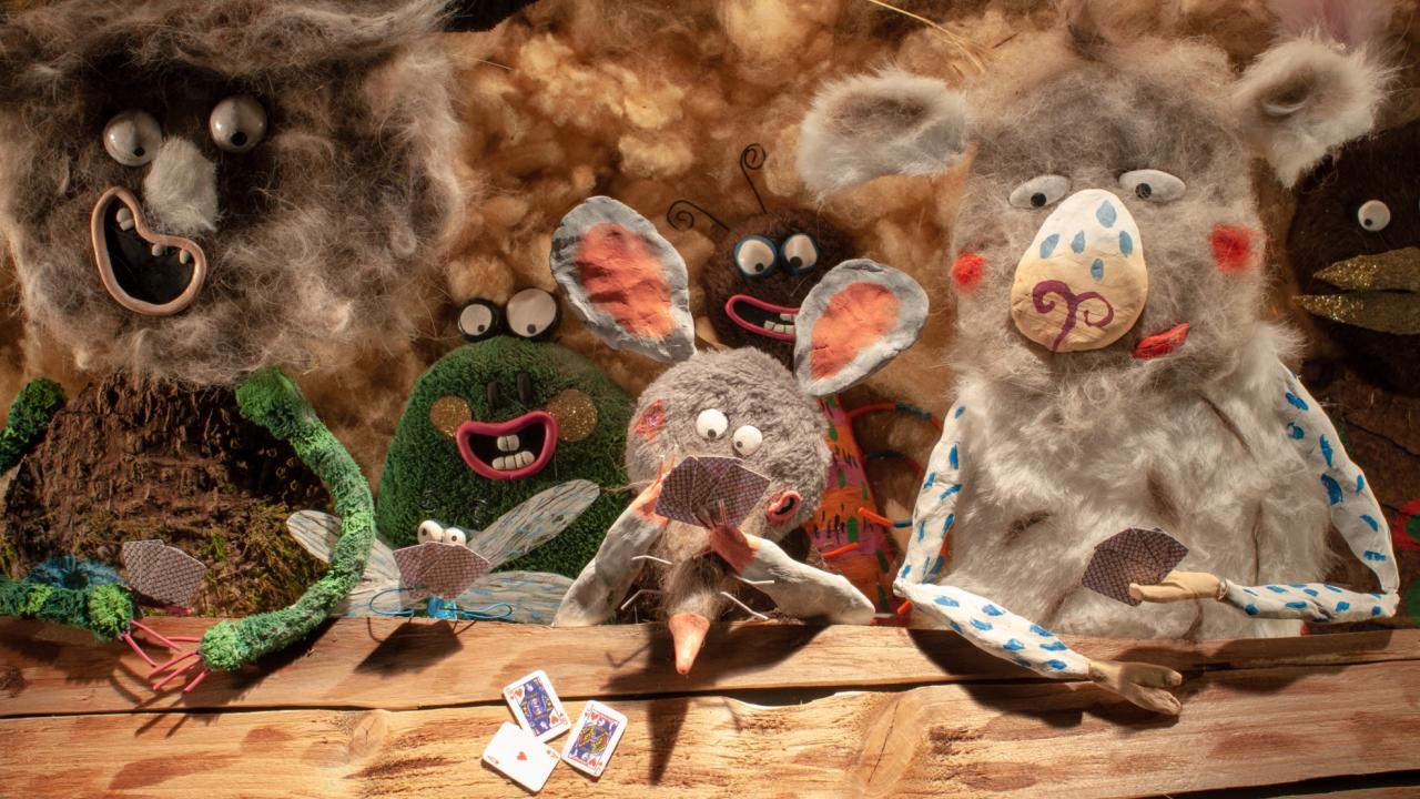 Still aus dem Animationsfilm CŒUR FONDANT: Vier im Legetrick animierte Tierfiguren sitzen am Tisch und spielen Karten. Ihnen schauen zwei weitere Gestalten über die Schulter.