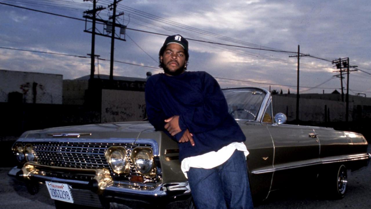 Still aus dem Drama BOYZ N THE HOOD: Ein junger Schwarzer, gespielt von Ice Cube, steht vor dramatischen Himmel vor einem Cabriolet.