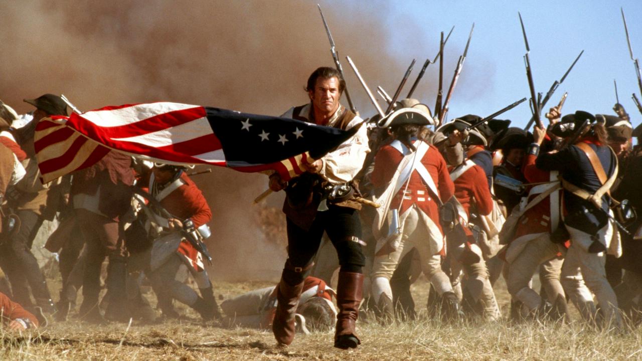 Still aus dem Historiendrama DER PATRIOT: Während des Unabhängigkeitskriegs rennt ein Mann mit einer amerikanischen Flagge auf die Kamera zu. Im Hintergrund sind Kampfszenen.