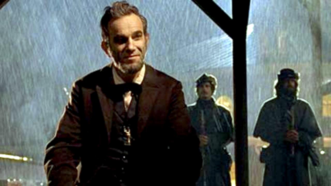 Still aus dem Biopic LINCOLN: Die Titelfigur sitzt nachts bei Regen unter einem Dach. Im Hintergrund stehen zwei Soldaten.