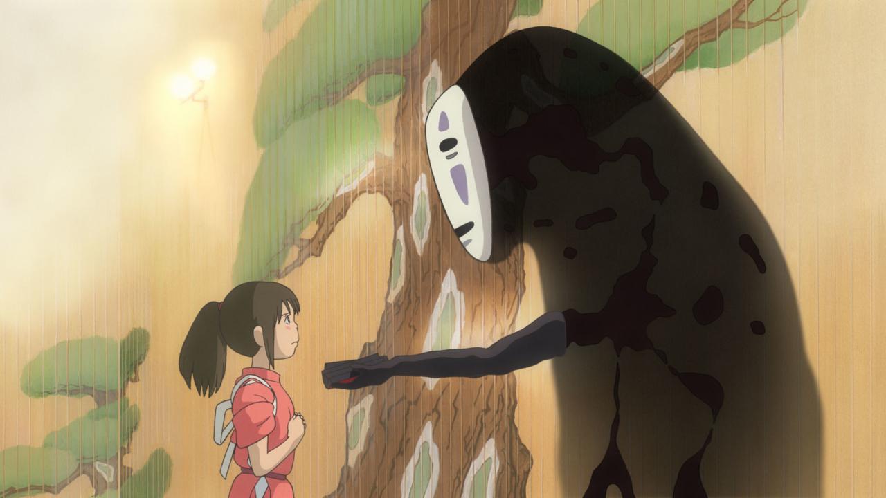 Still aus dem japanischen Anime CHIHIROS REISE INS ZAUBERLAND: im Profil ist ein rot gekleidetes Mädchen zu sehen, das einer schwarzen, doppelt so großen Gestalt mit einer weißen Gesichtsmaske gegenübersteht. Die Gestalt reicht dem Mädchen die Hand. Im Hintergrund ist eine mit einem Baum bemalte Wand zu sehen.