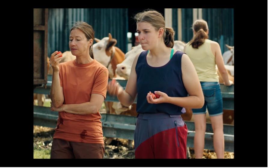 Screenshot aus MILCH INS FEUER: Katinka und ihre Mutter stehen vor dem Stall, machen Pause und essen Tomaten.