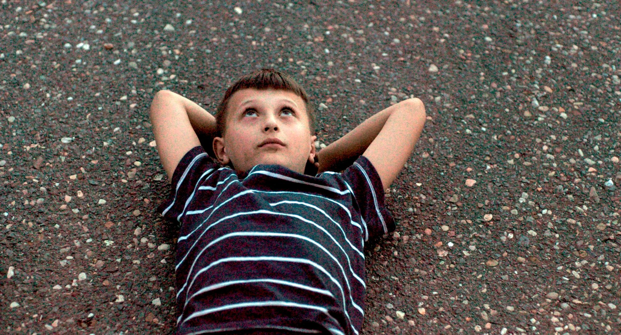 Still aus dem Dokumentarfilm ZIRKUSKIND: Der elfjährige Santino, Hauptfigur des Films, liegt auf dem Boden und schaut nach oben.