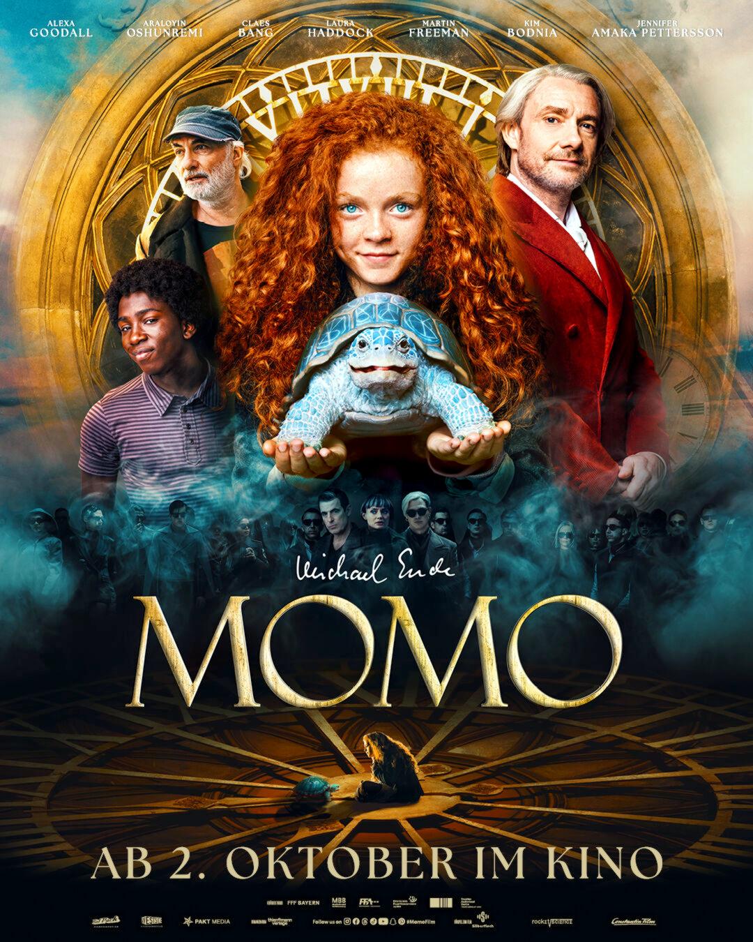 Plakat zum Spielfilm MOMO: Zentral ist ein rothaariges Mädchen zu sehen, das vor sich eine Schildkröte hält und lächelt. Um sie herum sind Männerfiguren angeordnet vor einem goldenen Kreis. Darunter steht in goldenen Buchstaben steht der Filmtitel.