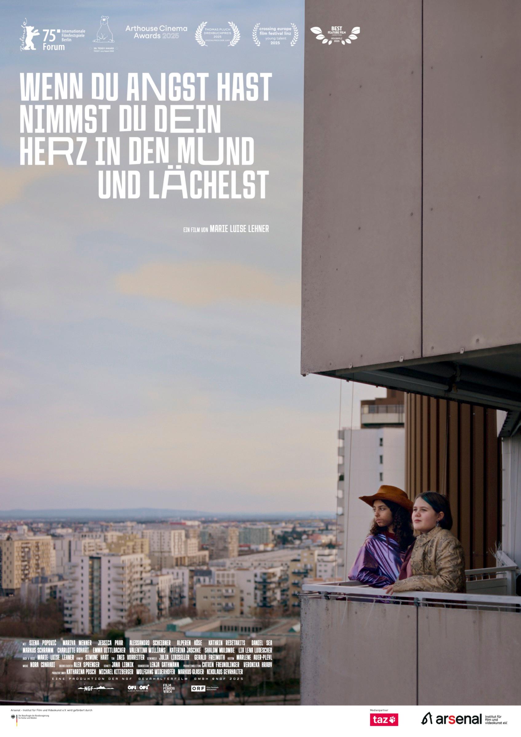 Plakat zum Drama WENN DU ANGST HAST NIMMST DU DEIN HERZ IN DEN MUND UND LÄCHELST: Zwei Mädchen im Teenageralter stehen auf einem Balkon vor einem weiten Stadtpanorama.