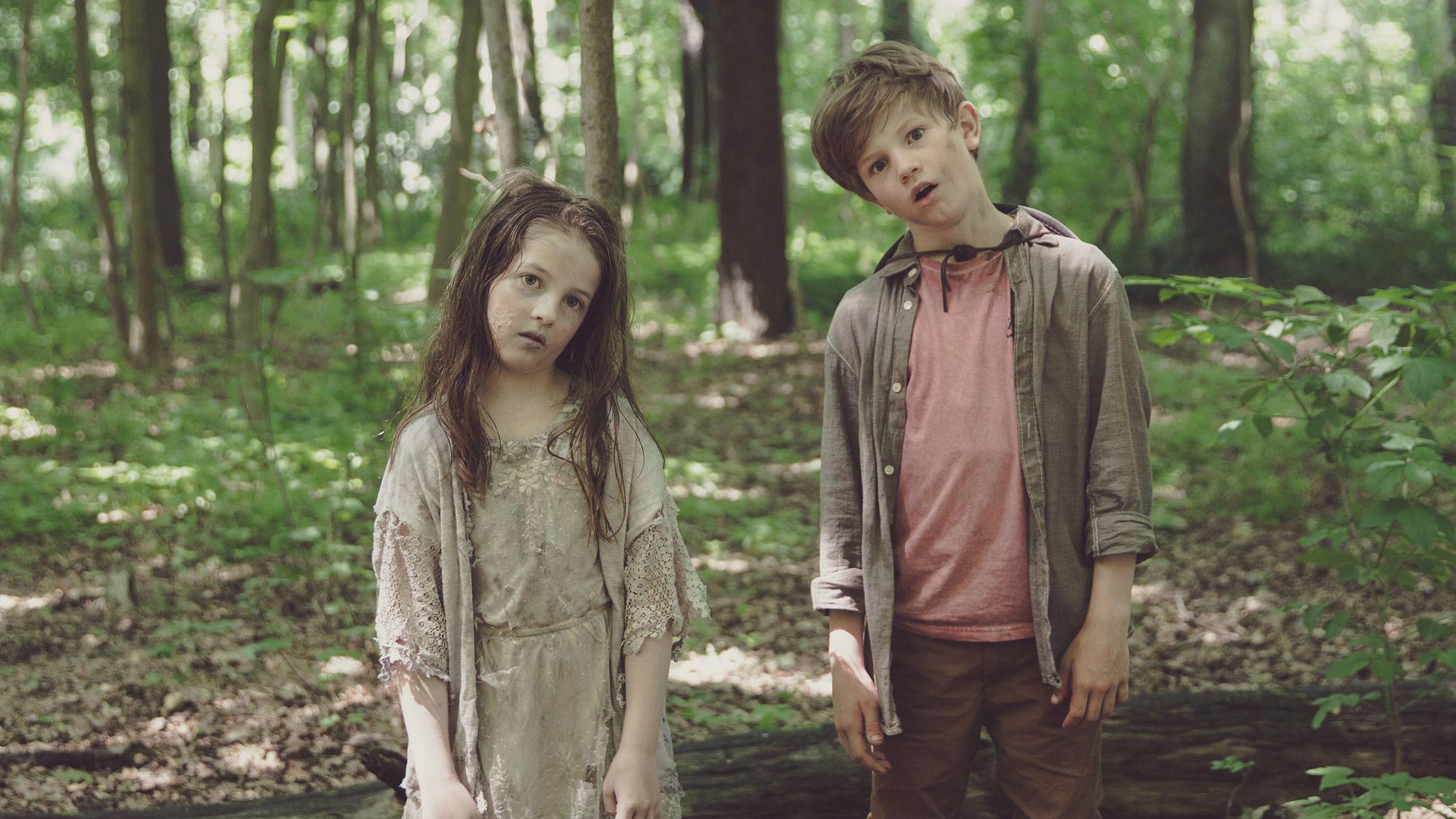 Stil aus dem Kurzfilm ZOMRIELLA: Ein Junge und ein ungewöhnlich blasses und zerzaustes Mädchen stehen mit seltsam seitlich gekippten Köpfen im Wald und schauen in Richting Kamera.