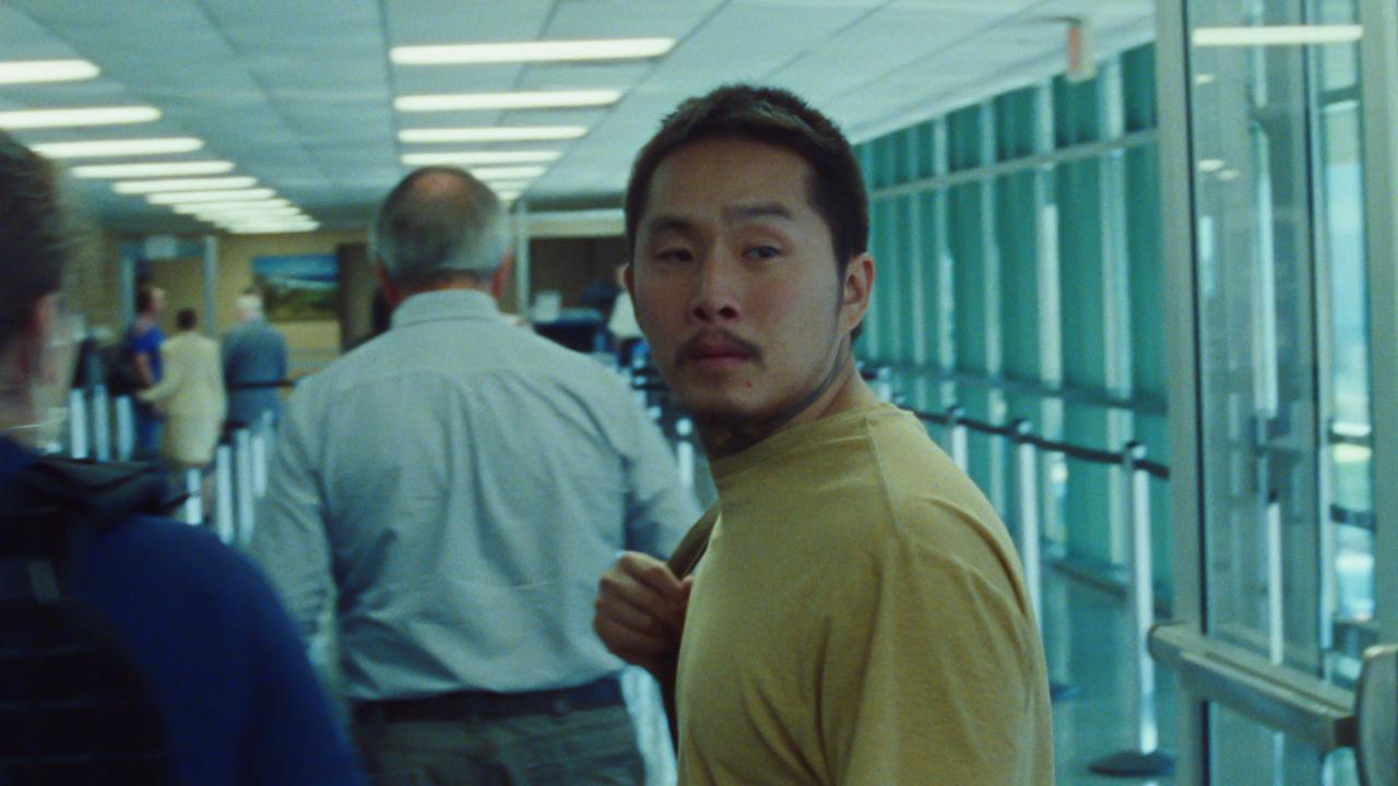 Ein Mann mit gelben T-shirt und asiatischen Gesichtszügen dreht sich in einem Gang um.