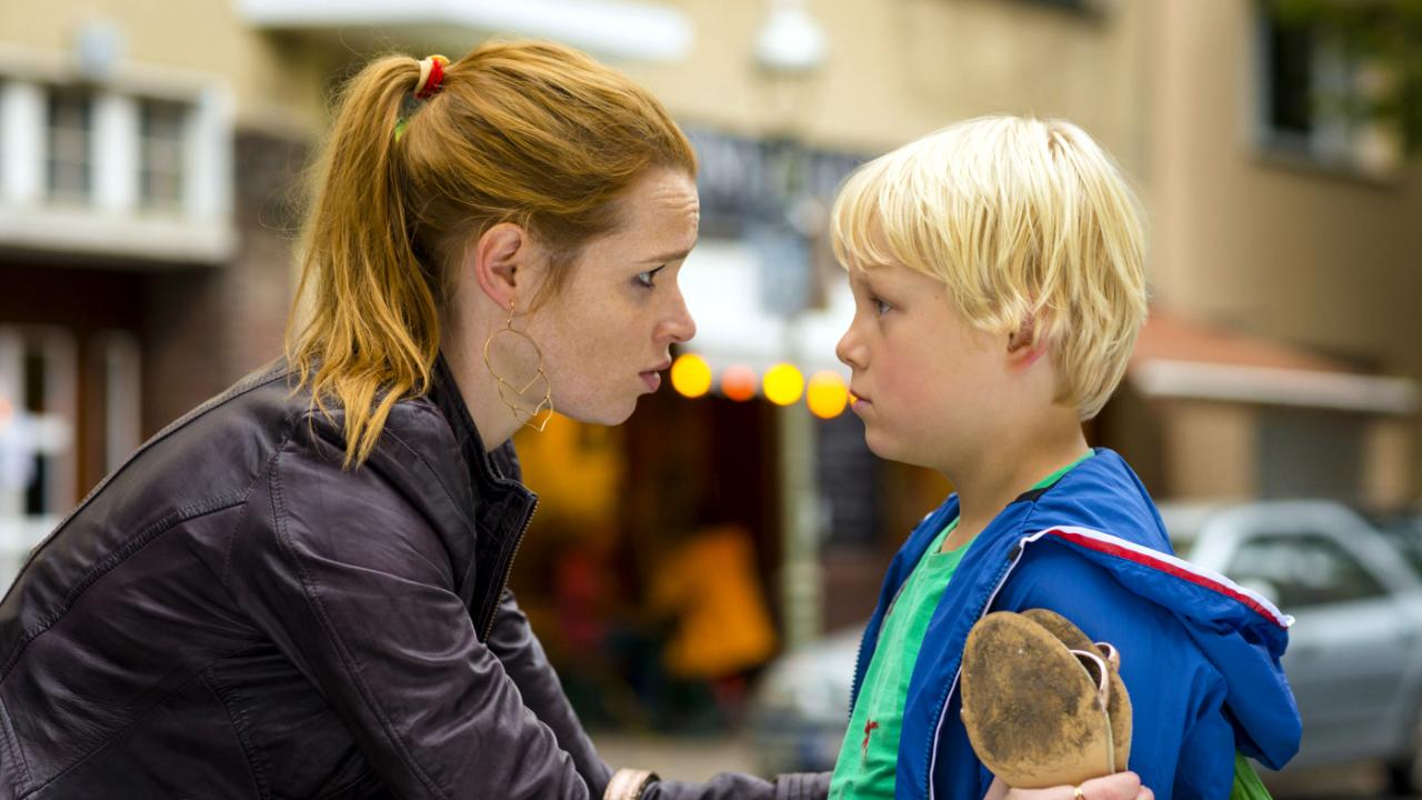 Szenenbild aus dem Film "Rico, Oskar und die Tieferschatten": Nahaufnahme: Eine junge Frau mit Pferdeschwanz beugt sich leicht zu einem blonden Jungen herunter und hält ihn an den Armen fest.