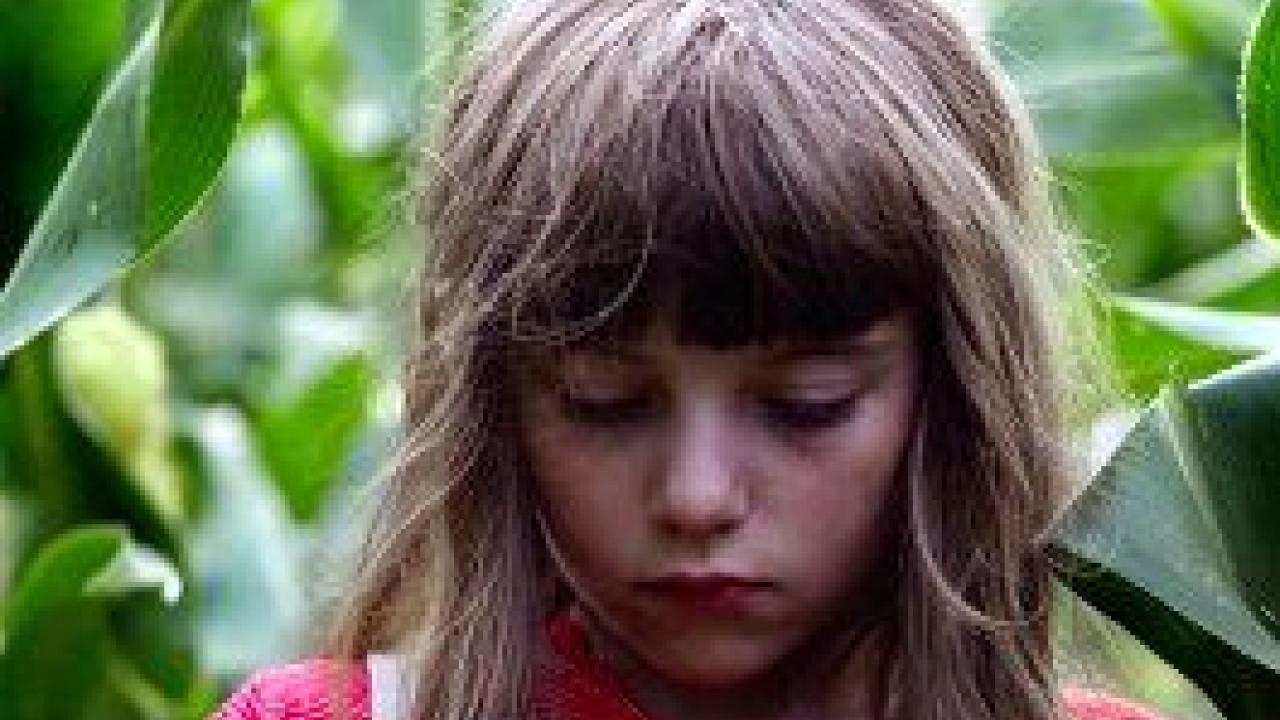 Nahaufnahme: Ein Mädchen mit Pony steht zwischen Pflanzen und guckt nach unten
