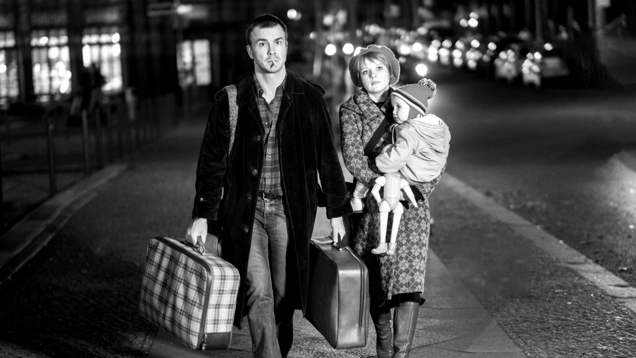 Szenenbild aus dem Biopic "Lieber Thomas": Ein Mann und eine Frau gehen nachts durch Berlin. Er trägt einen Koffer, sie ein Kind im Arm. Sie schauen ernst. 