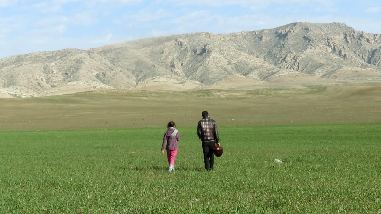 Totale: ein grünen Feld mit Berge im Hintergrund. Zwei Figuren laufen den Bergen entgegen: ein Mädchen und ein Mann.