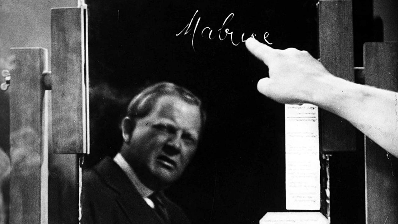 Szenenbild aus dem Drama DAS TESTAMENT DES DR. MABUSE: Ein Mann beobachtet, wie eine Hand das Wort "Mabuse" auf einen Spiegel schreibt.