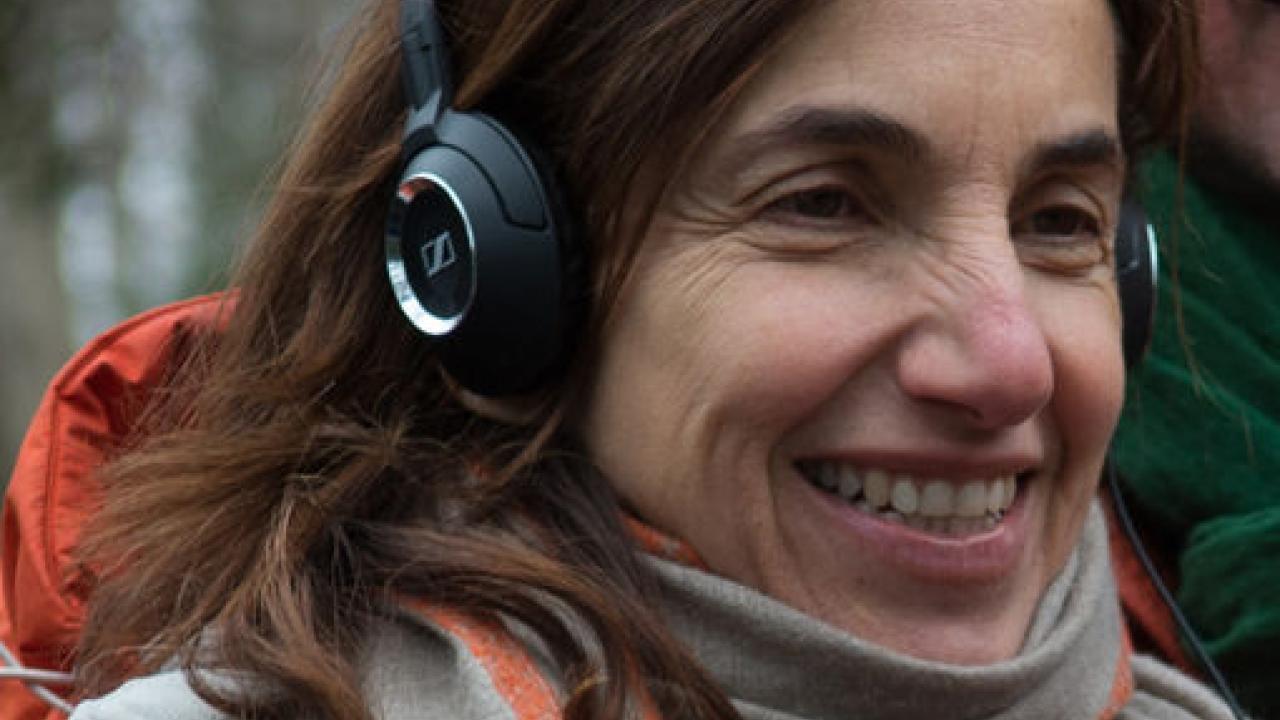 Regisseurin Gaby Dellal hat Kopfhörer auf und lächelt. 