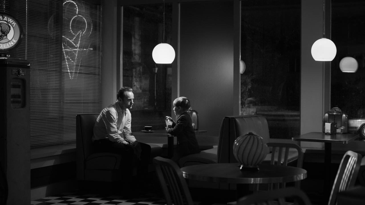 Der Geburtstag, Szenenbild in Schwarz-Weiß: Ein Mann und ein Junge sitzen nachts in einem Café. 