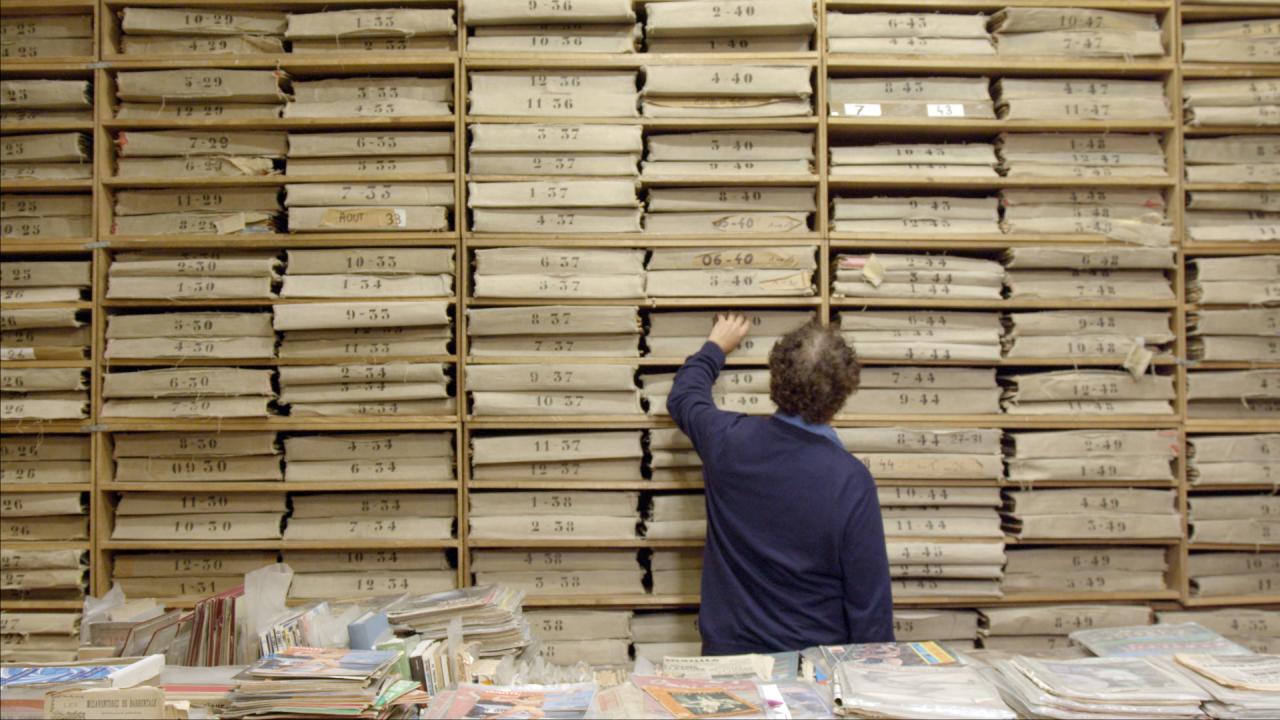 Szenenbild aus dem Dokumentarfilm DIE ROTE KAPELLE:  Der Historiker Guillaume Bourgeois steht vor einer Wand voller Akten. Er steht mit dem Rücken zur Kamera.