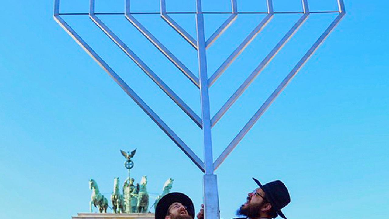 Germans & Jews, Szenenbild: Zwei jüdisch-orthodoxe Männer errichten in Berlin vor dem Brandenburger Tor einen riesigen Chanukka-Leuchter