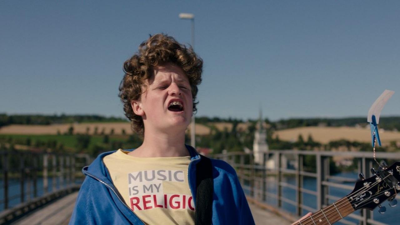 Thilda & die beste Band der Welt, Szenenbild: Nahaufnahme des rothaarigen Lockenkopfs Aksel, der auf einer Brücke steht und voller Inbrunst singt. Auf sein T-shirt steht "Music is my religion".