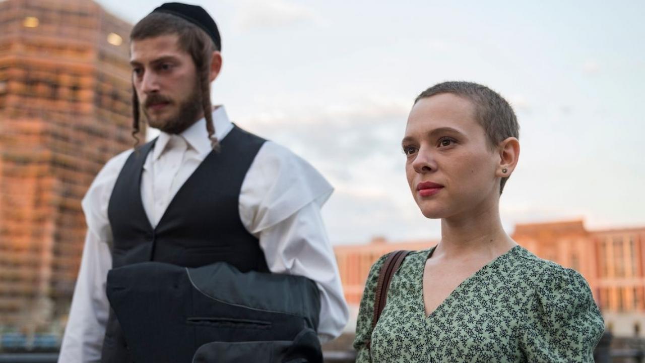 Unorthodox, Szenenbild: Eine jungem kurzhaarige Frau läuft neben einem jungen jüdisch-orthodoxen Mann.