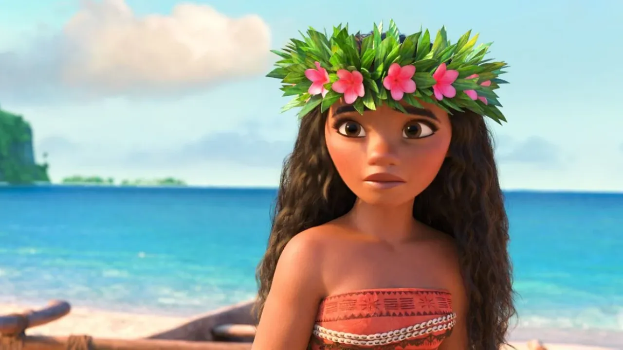 Vaiana, Szenebild: in Animation, ein junges Mädchen mit längen braunen Haaren und Blumenkronen steht an einem idyllischem Strand und guckt besorgt.
