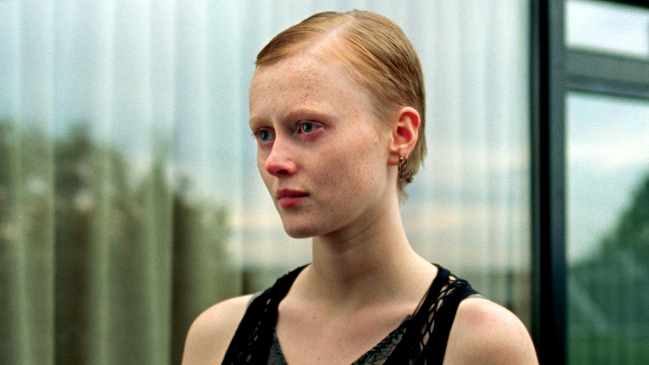 Still aus dem Drama WENN DAS LICHT ZERBRICHT: Porträt einer jungen Frau mit kurzen Haaren und ernsten Gesicht. Sie steht vor einer großen Fensterscheibe, in der sich die Landschaft spiegelt.