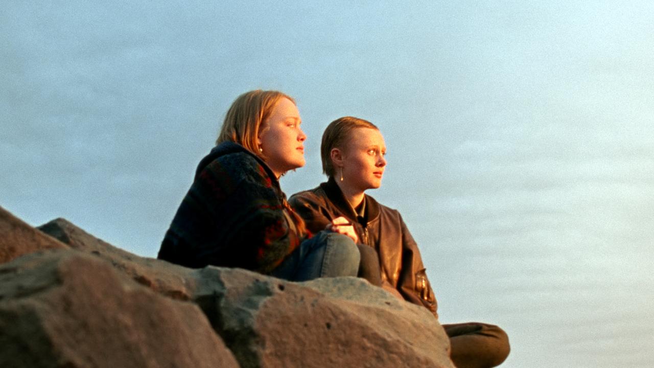Still aus dem Drama WENN DAS LICHT ZERBRICHT: Zwei jungen Frauen sitzen vor weitem Himmel auf einem Felsen und blicken nach rechts in die Ferne.