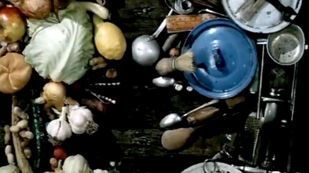 Screenshot aus dem Kurzfilm TÜCKEN DES GESPRÄCHS: Zwei Gesichter – das eine aus verschiedenen Gemüsesorten, das andere aus Küchenutensilien zusammengestellt – stehen sich gegenüber.