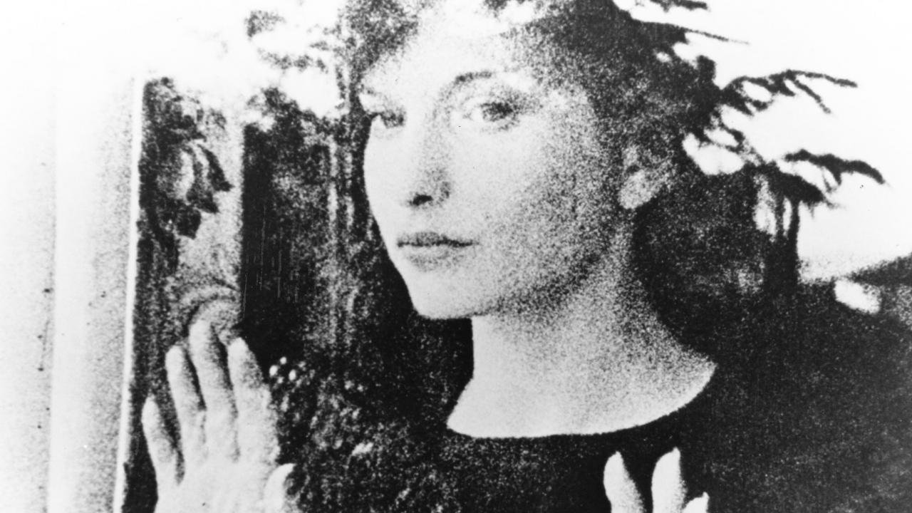 Filmstill aus MESHES OF THE AFTERNOON: Bild einer Frau hinter einer Fesnterscheibe: Sie hält die Hände an das Glas und schaut hinaus. Die Außenwelt spiegelt sich im Glas.