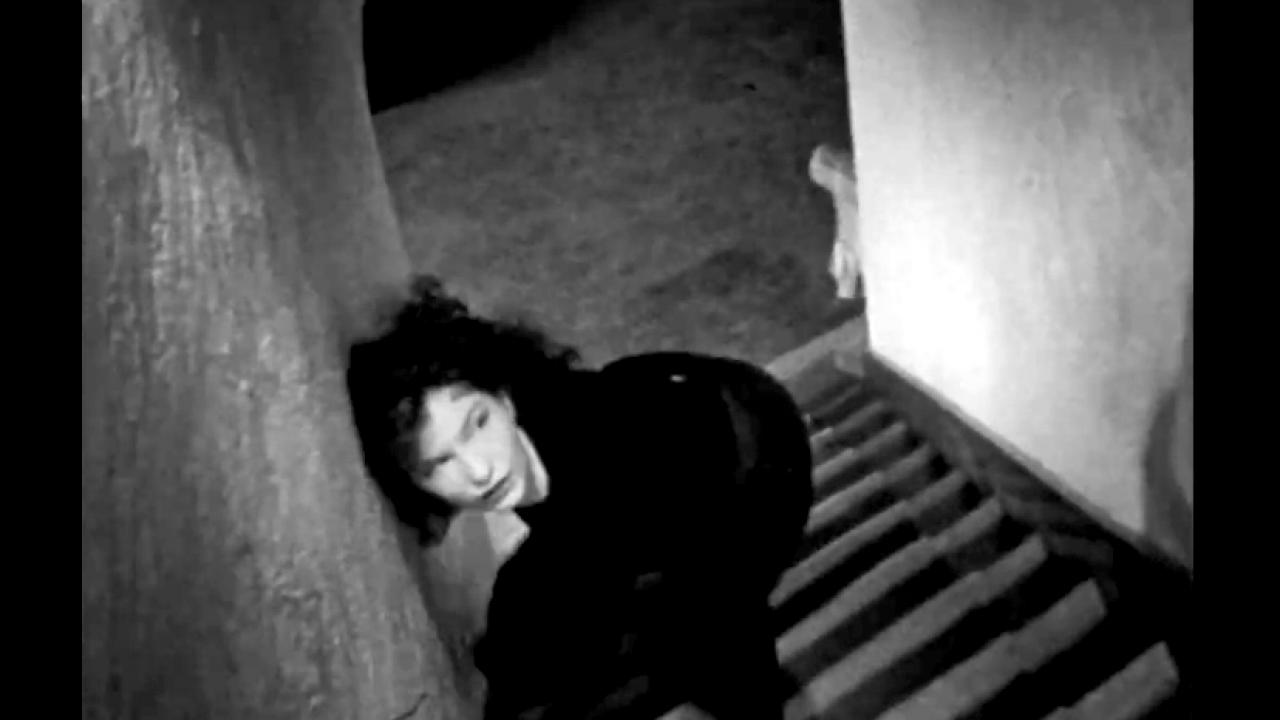 Screenshot aus dem Kurzfilm MESHES OF THE AFTERNOON: Eine Frau taumelt eine Treppe hoch. Ihr Kopf liegt an der Wand.