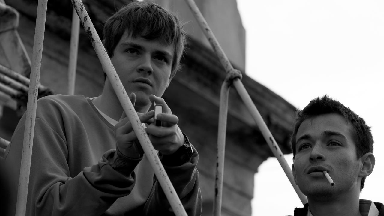 Filmstill aus dem Drama YURT: Zwei Jungen im Teenageralter sitzen nebeneinander und schauen in die Ferne. Ein Junge raucht. Das Bild ist in Schwarz-Weiß aufgenommen.