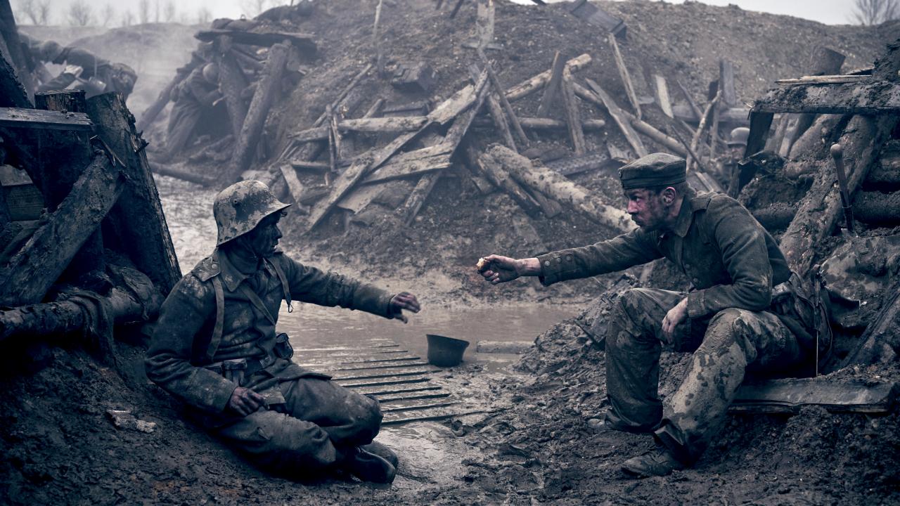 Still aus dem Kriegsdrama IM WESTEN NICHTS NEUES: Zwei Soldaten sitzen im Ersten Weltrkieg in einem Schützemgraben gegenüber und strecken die Hände aus. Es hat geregnet, alles ist voller Matsch.