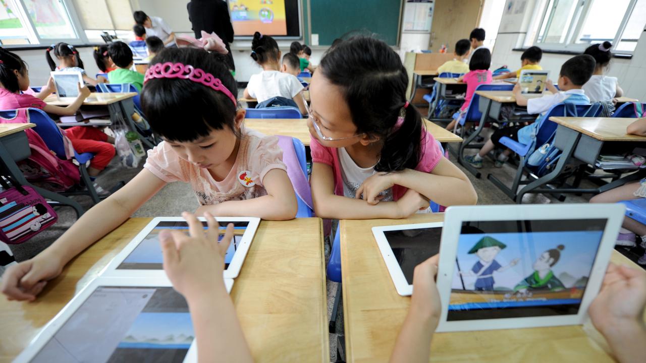 Kinder sitzen in einem Klassenraum und arbeiten mit Tablets.