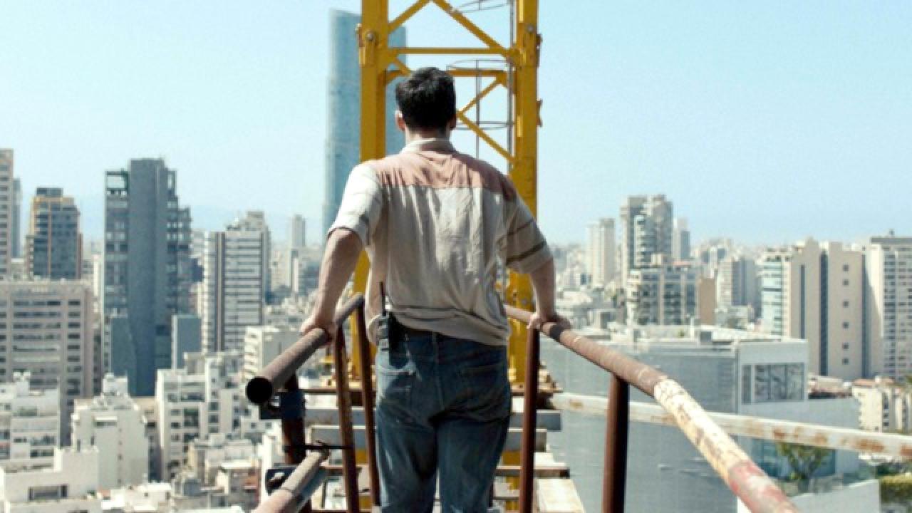 Still aus dem Kurzfilm HOCH OBEN: Ein Mann, in der Rückenansicht zu sehen, geht über eine Stiege auf einen Kran zu. Um ihn herum ist die Skyline von Beirut zu sehen.