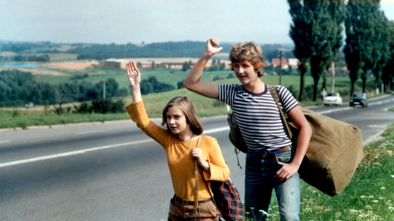 Filmstill aus dem Roadmovie TRAMPEN NACH NORDEN: Ein Junge und ein Mädchen, beide im Teenageralter, stehen an einer Landstraße und versuchen per Handzeichen eine Mitfahgelegenheit zu bekommen.