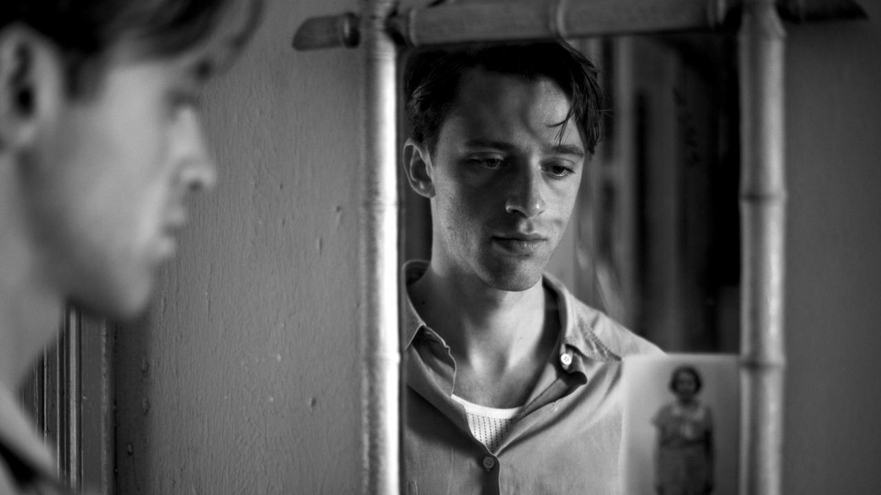 Filmstill aus DER FREMDE: Ein junger Mann steht vor einem Spiegel, sein Spiegelbild steht im Zentrum des schwarz-weißen Bildes.