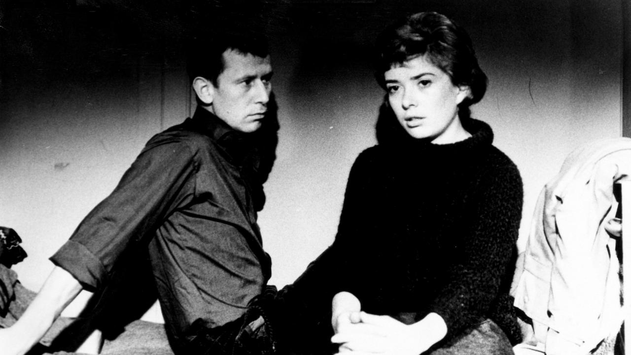 Filmstill aus dem DEFA-Drama SPUR DER STEINE: Eine junge Frau und ein junger Mann sitzen auf einem Buch. Die Frau schaut nach vorne, der Mann schaut sie an.