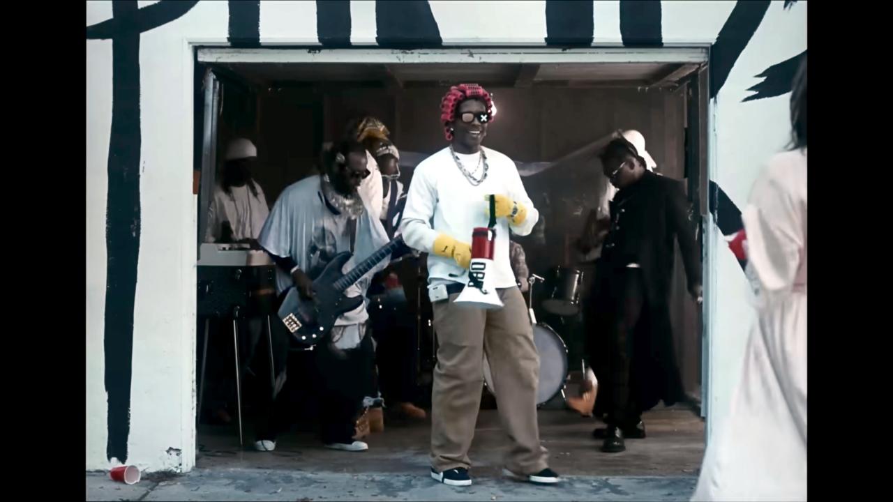 Screenshot ais dem Musikvideo PUNK ROCKY von A$AP Rocky: Der Sänger steht im Tor einer Garage, er hält ein Megaphon in der Hand. Hinter ihm stehen Schwarze Musiker.